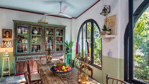 Un coin repas comprenant une table en bois, des chaises, un panier de fruits, une lampe ancienne et un buffet vert aux portes en verre.