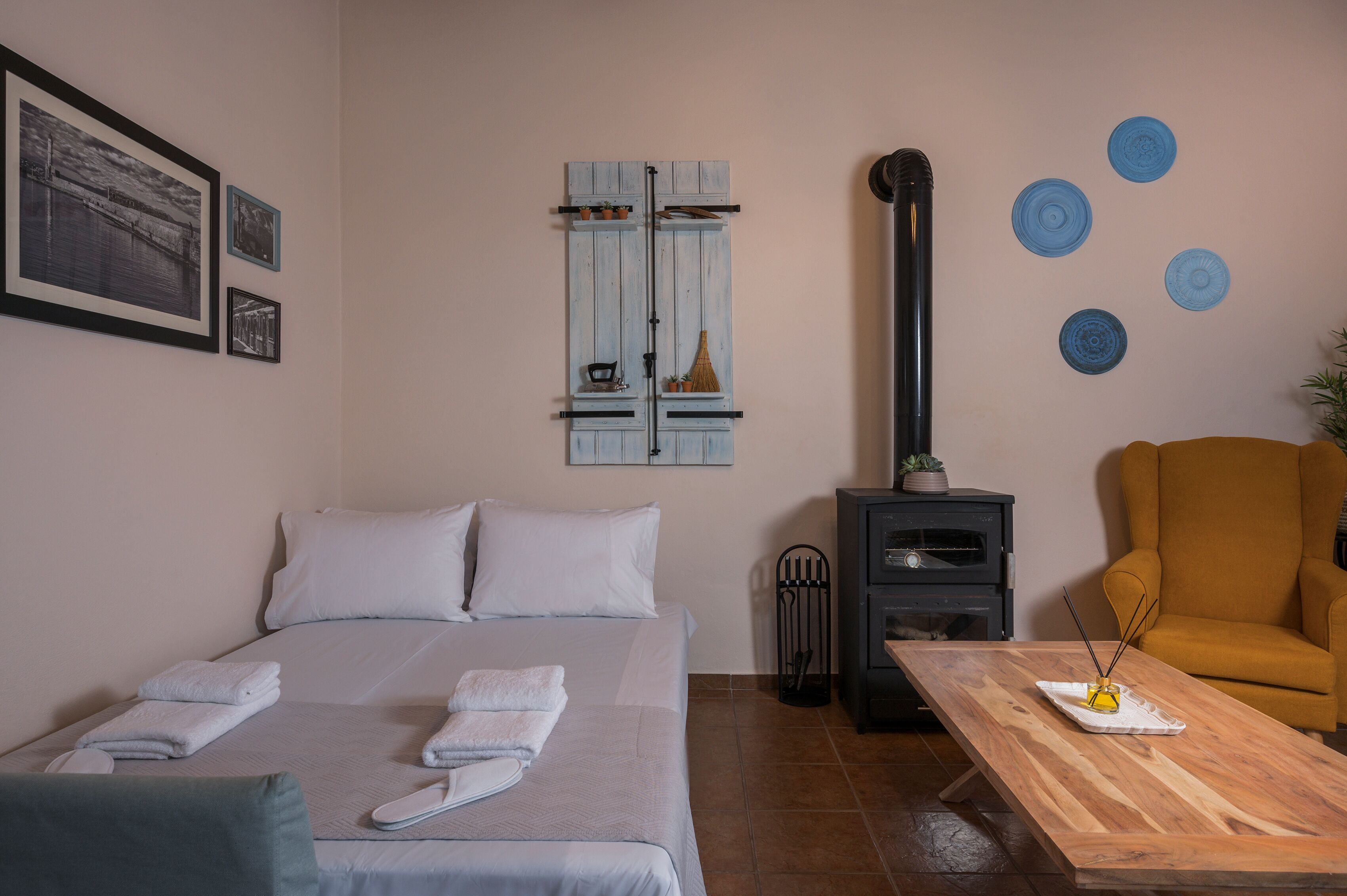 Una camera da letto con un letto, un tavolo in legno, una poltrona gialla, un termosifone nero e decorazioni alle pareti.