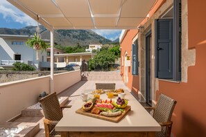 A terrace with a table set for breakfast, including fruits and pastries, overlooking a mountainous landscape. - Iosif De Home (Apokoronas)