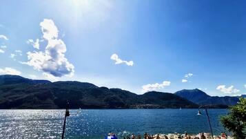 Una spiaggia con persone che prendono il sole e nuotano, circondata da montagne e un cielo sereno.