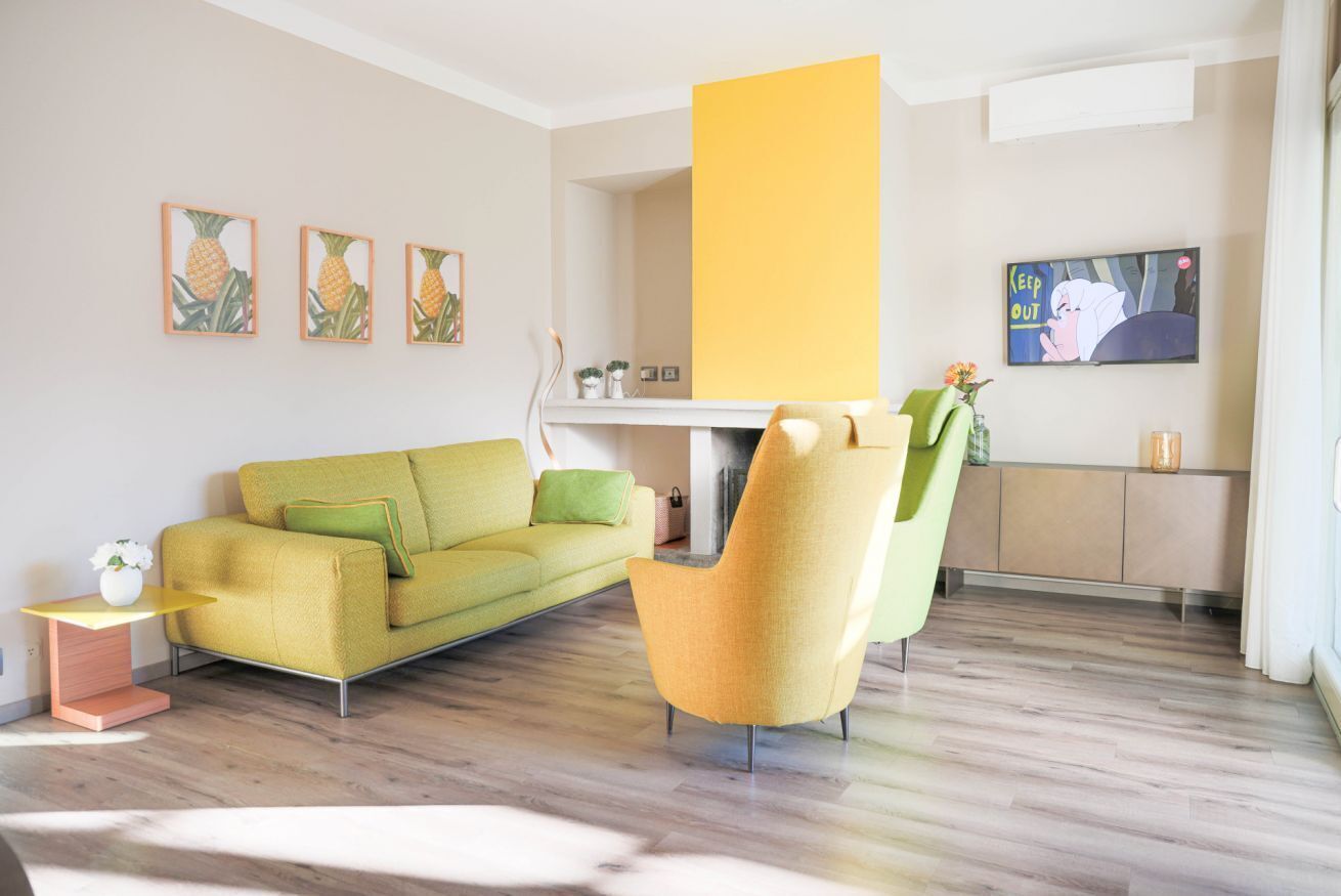 Un soggiorno moderno con un divano verde, una poltrona gialla e una televisione a schermo piatto appesa al muro.