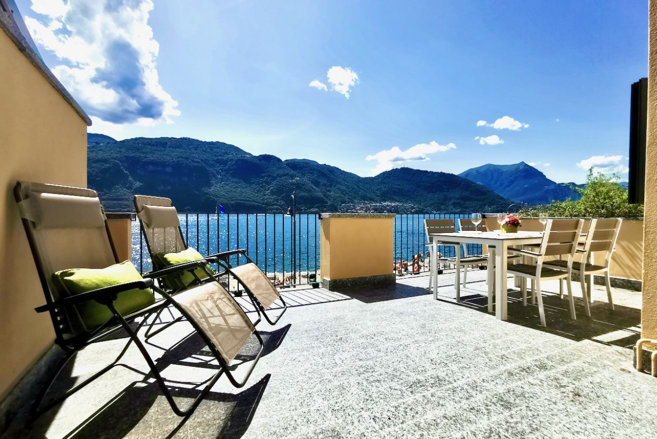 Eine Terrasse mit Stühlen und einem Tisch mit Blick auf einen See und Berge.