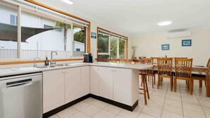 A compact kitchen with a dishwasher, a sink, and a dining area with wooden chairs and a table.