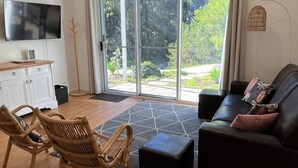 A modern living room with a sofa, chairs, a TV, and a view of a garden through large sliding doors.