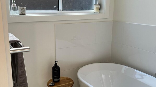 Un baño con una bañera, un perchero, un taburete de madera y una botella de jabón de ducha.