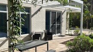 A patio area with a table and chairs, a grill, and a covered seating area with a view of the surrounding greenery.