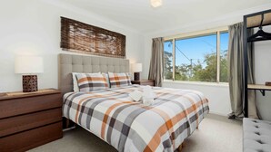 A bedroom with a large bed, two bedside tables, a hanging wardrobe, and a window with curtains. - Our Beach House by Experience Jervis Bay (Vincentia)
