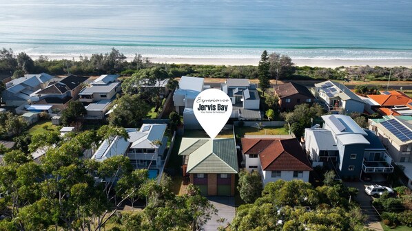 An aerial view of a residential area with houses, solar panels, and a beach in the background.