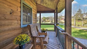 A wooden porch with a bench and potted plants, overlooking a green landscape.