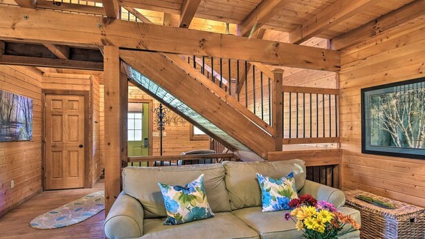 A cozy cabin interior with a wooden staircase, a sofa with floral cushions, and a vase of flowers.