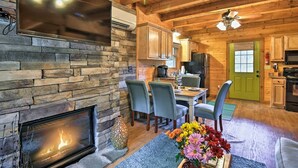 A cozy cabin interior with a stone fireplace, dining area, and kitchen.