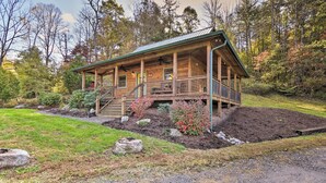 A wooden cabin with a porch, surrounded by a landscaped garden with various plants and a small hill.
