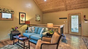A cozy living room with a wooden ceiling, a blue sofa, a striped armchair, and a small side table with a lamp. - Chanterelle Cabin w/Hot Tub, Fireplace - Near Asheville! (Weaverville)