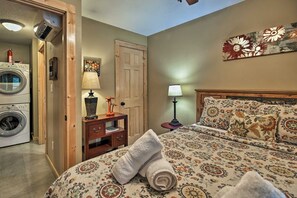 A bedroom with a bed, a nightstand, a lamp, a wall-mounted artwork, a door, and a washing machine. - Chanterelle Cabin w/Hot Tub, Fireplace - Near Asheville! (Weaverville)