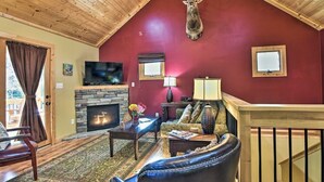 A cozy living room with a stone fireplace, a mounted deer head, a television, and comfortable seating.