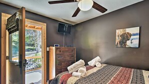 A bedroom with a bed, a wooden dresser, a television, and a painting on the wall.