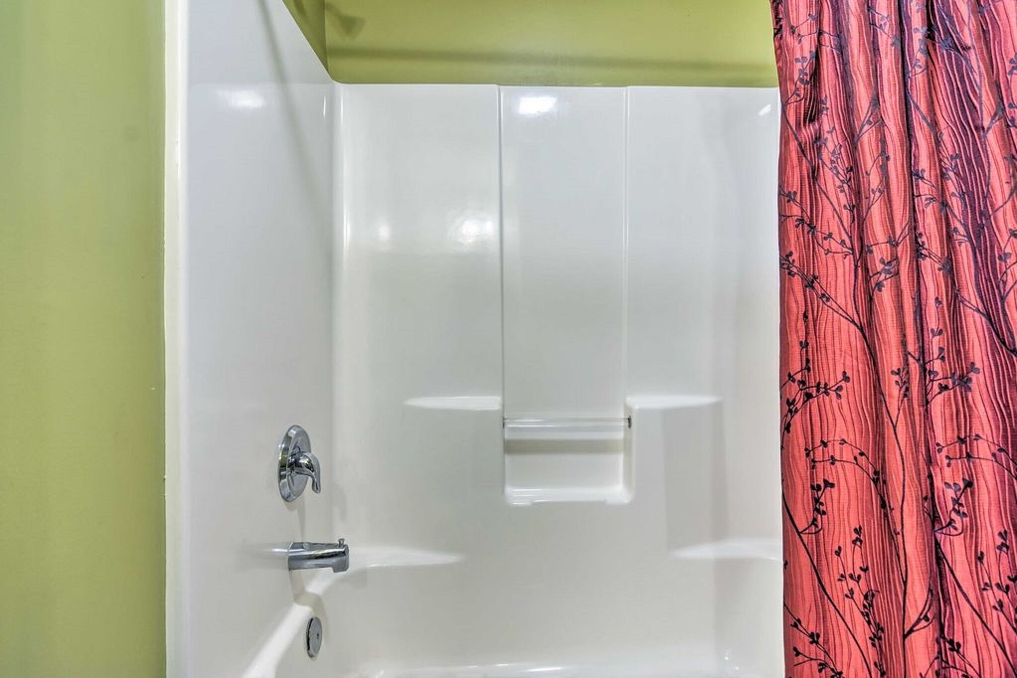 A bathroom with a white bathtub, a chrome faucet, and a green wall.