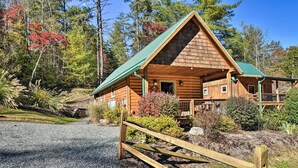 A log cabin with a green roof, a porch, and a gravel driveway.