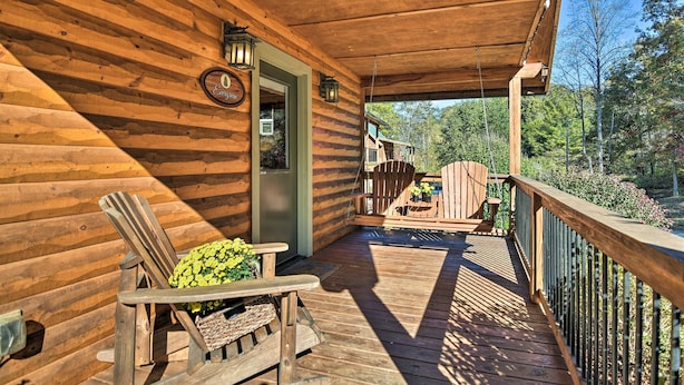 A wooden cabin with a covered porch, a chair with a cushion, and a view of the surrounding forest.