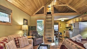 A cozy cabin interior with a loft bedroom, a dining area, and a kitchen.