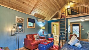 A cozy room with a red leather sofa, a blue ottoman, a patterned bedspread, and a wooden ceiling. - Dog-Friendly Weaverville Cabin King Bed,Hot Tub&FP (Weaverville)