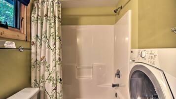 Un baño con ducha, inodoro y lavadora de carga frontal.
