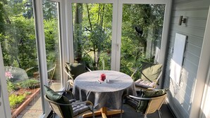 Un invernadero con una mesa redonda y cuatro sillas, ventanas amplias y vista a un jardín.