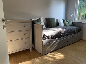 Una habitación compacta con cama, cómoda empotrada y ventana que proporciona luz natural.