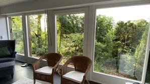 Una habitación moderna con ventanas amplias, sillas de mimbre, un sofá y un control remoto sobre una mesa.