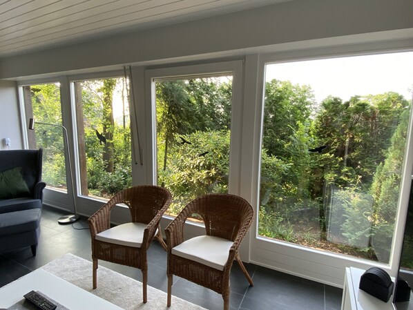 A modern room with large windows, wicker chairs, a sofa, and a remote control on a table.