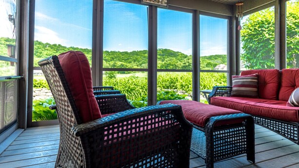 A covered outdoor seating area with wicker furniture and a red sofa, overlooking a lush green landscape. - Vista View | 3 Kings + 1 Queen | Hot Tub · Fire Pit · Fireplace (Galena)