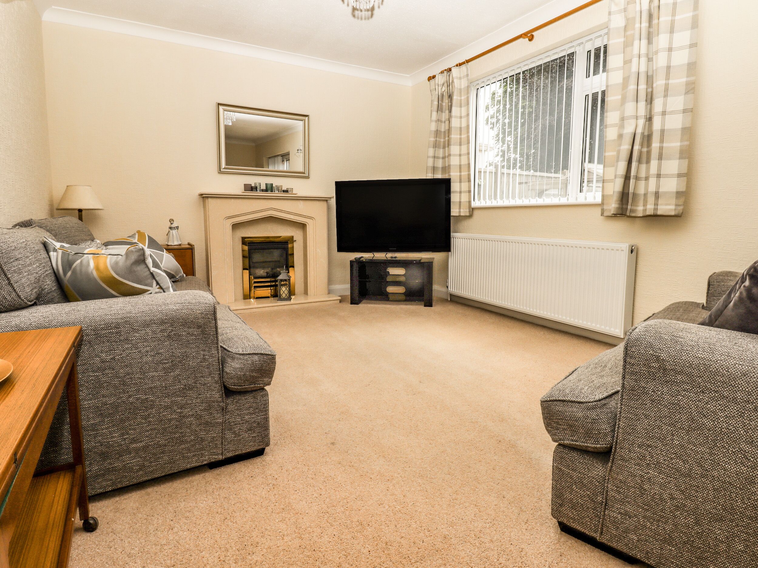 A living room with two grey sofas, a fireplace, a flat-screen TV, and a window with curtains.