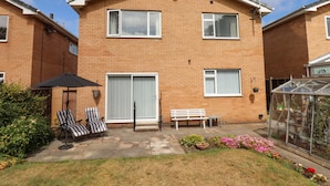 A two-story brick house with a patio area featuring a bench, two chairs, and a table.