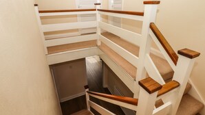 A narrow staircase with wooden handrails and beige carpeted steps.