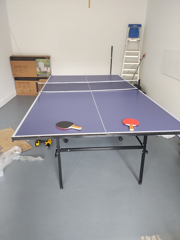 Una mesa de ping pong con dos palas, una escalera y algunas herramientas en el suelo.