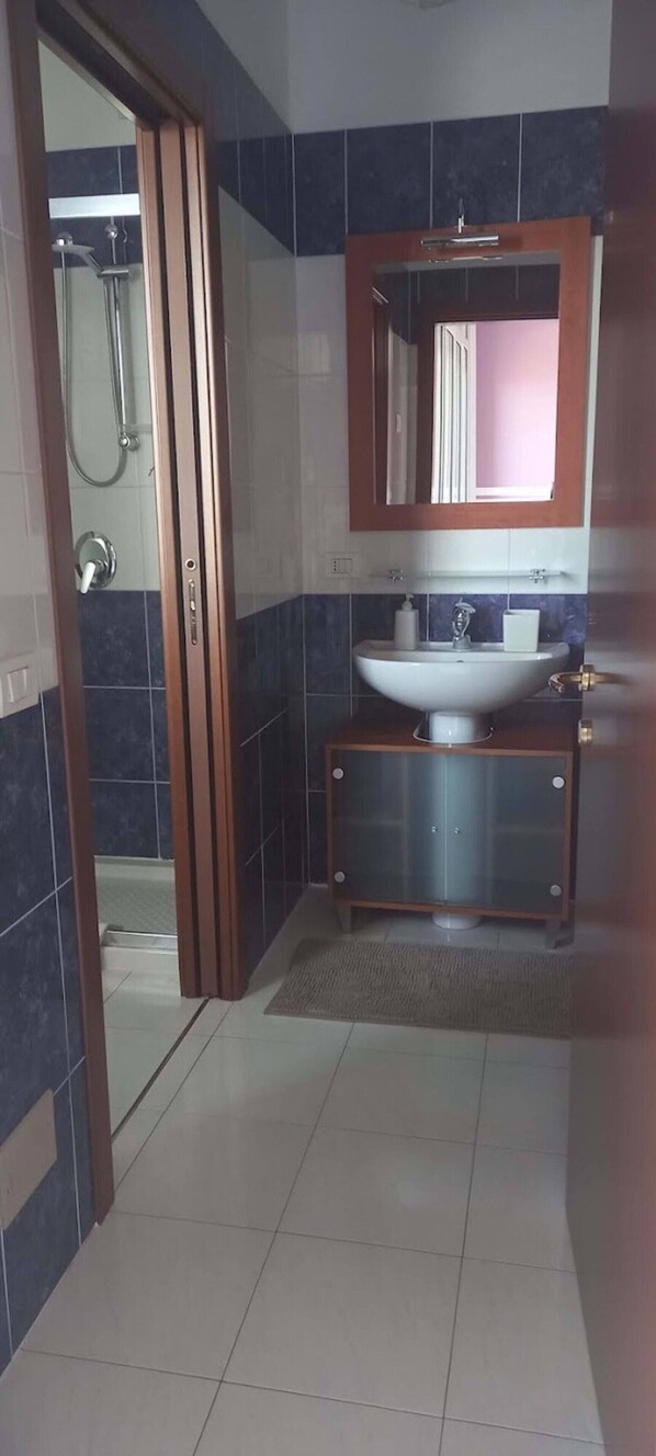 A bathroom with a glass shower enclosure, a white sink, and a wooden vanity.