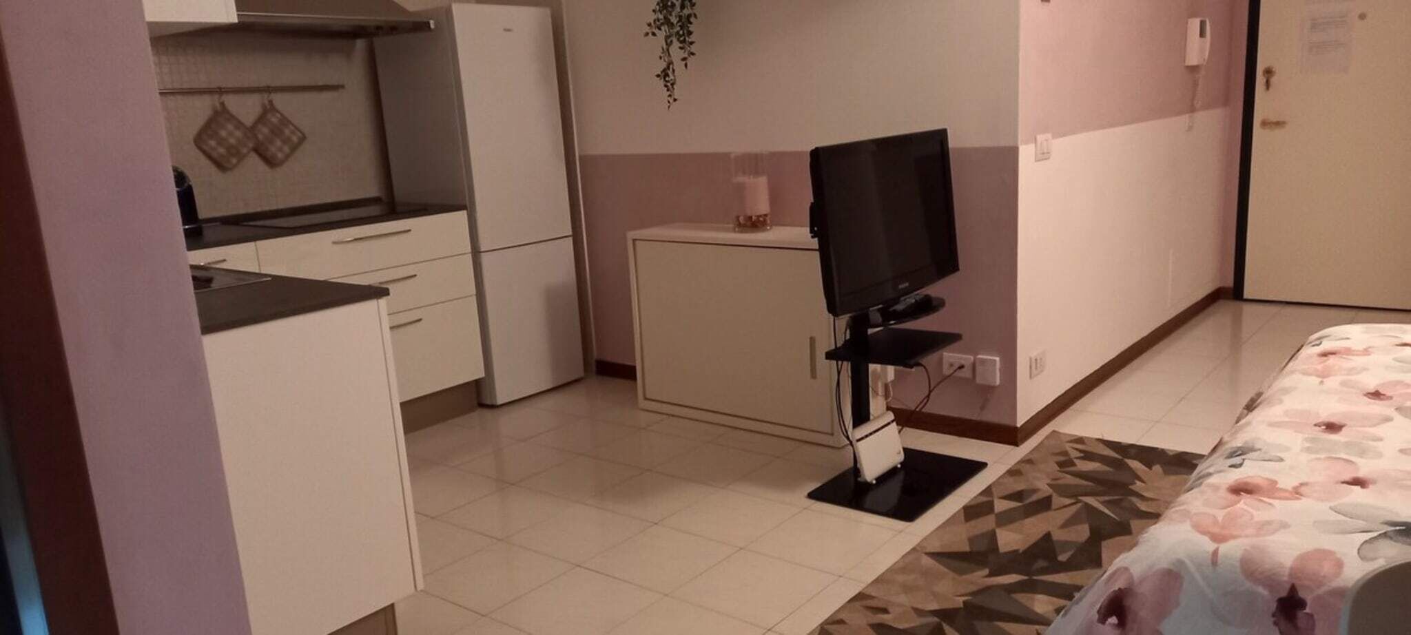 A compact room with a kitchenette, a flat-screen TV, and a bed with a floral bedspread.