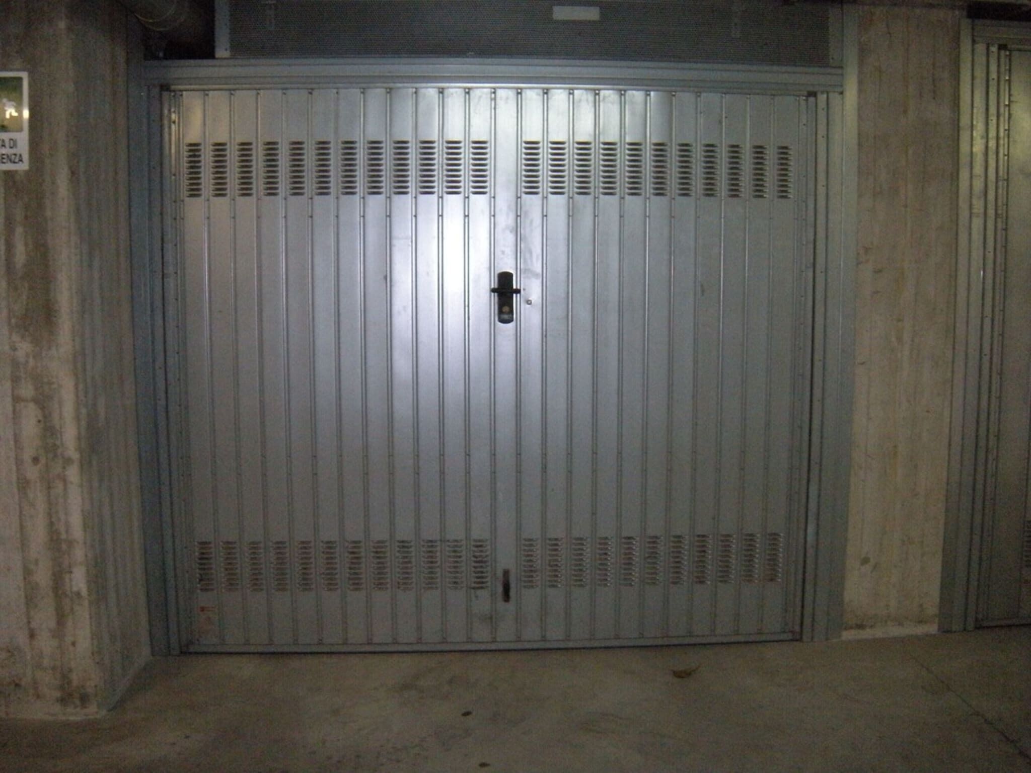 A large metal gate with a central lock, flanked by ventilation panels, and a concrete floor.