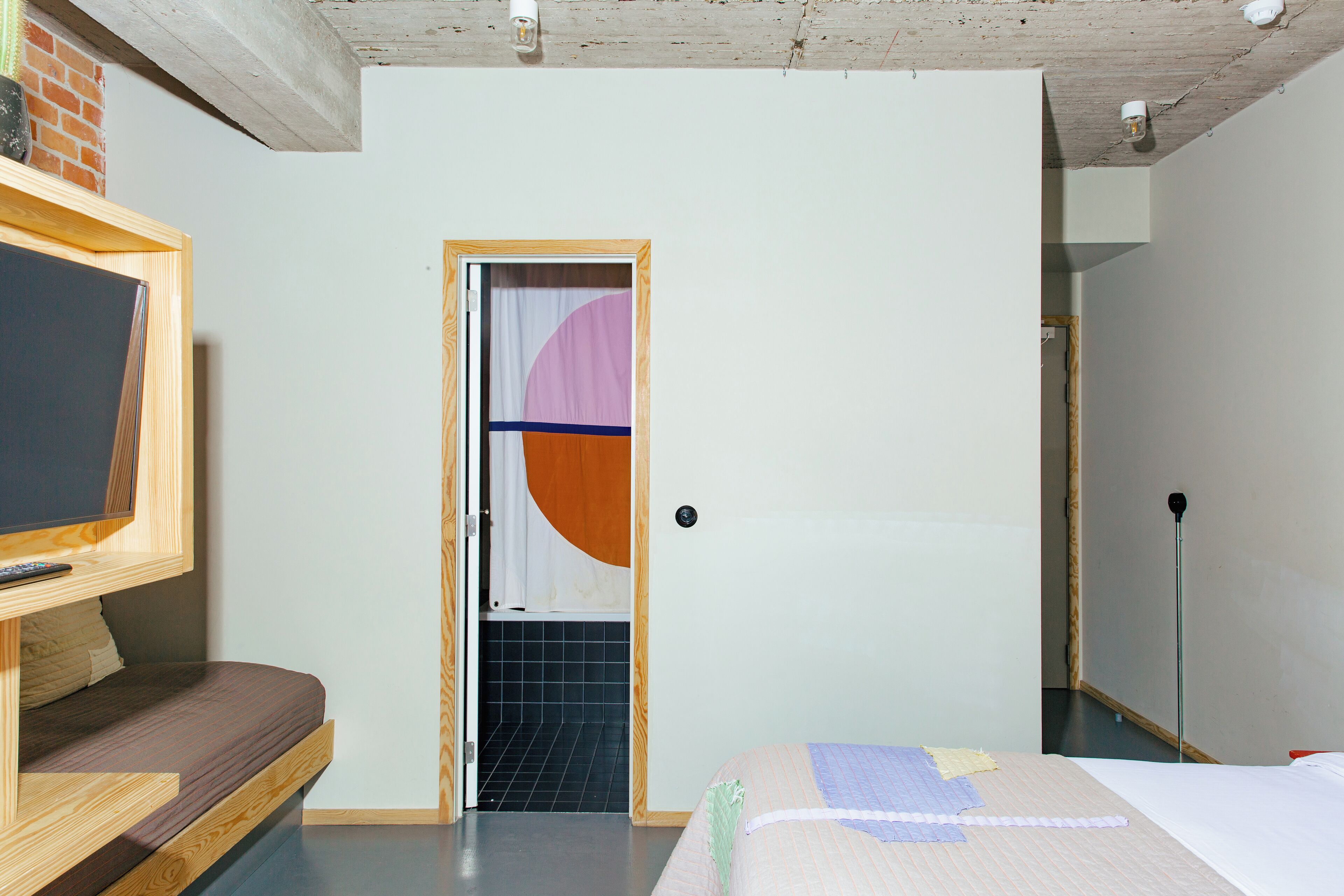 Une pièce avec un lit, une télévision et une porte qui donne sur une autre pièce.