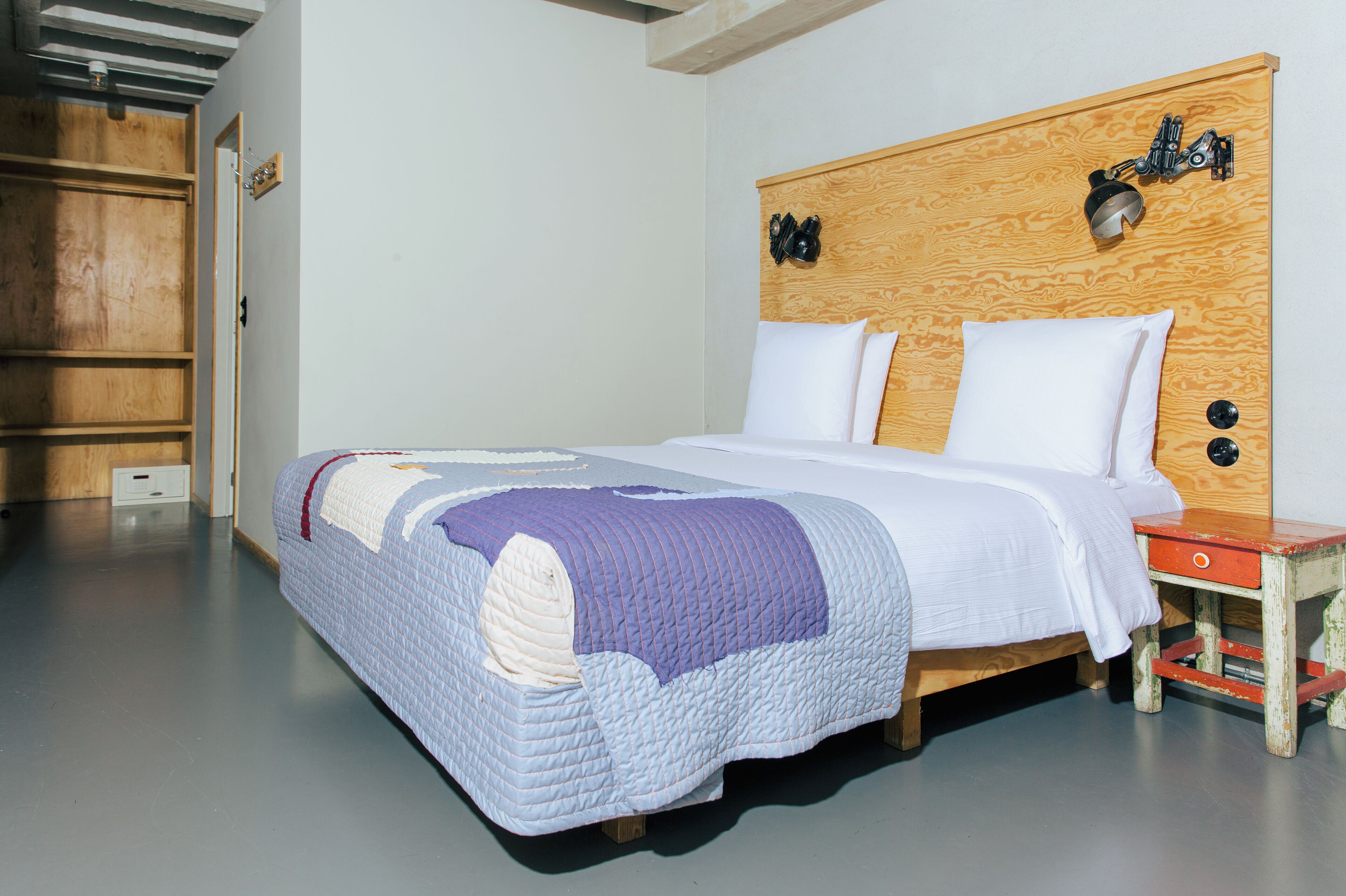 A neatly made bed with a wooden headboard, a bedside table, and a wooden wardrobe.