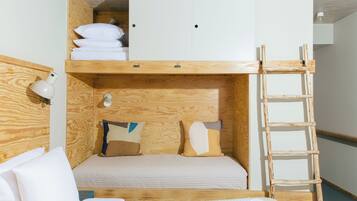 A bunk bed with a wooden ladder, a desk, and a lamp.