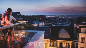 Un couple s’embrasse sur un balcon donnant sur une vue panoramique de la ville au crépuscule.