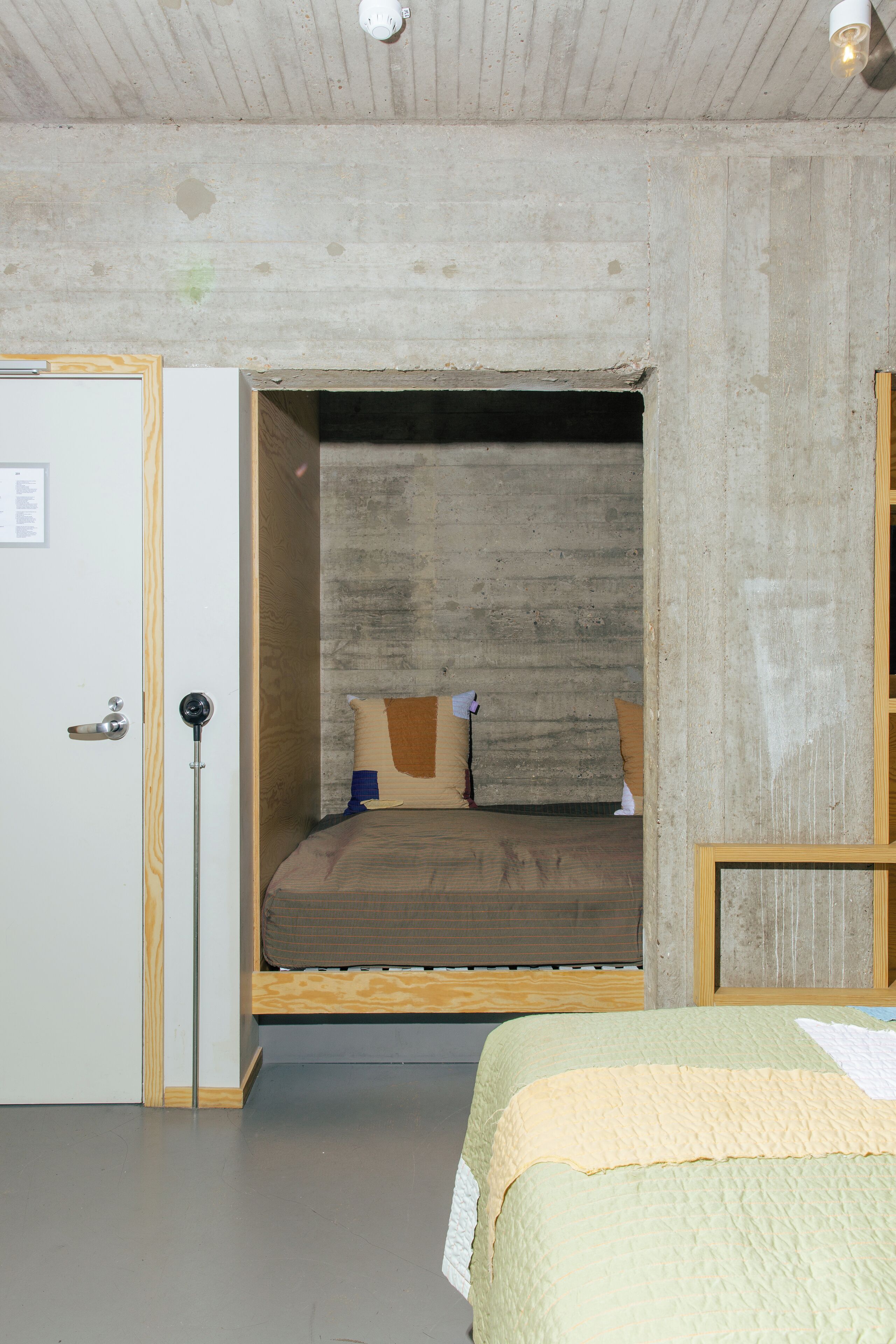 A room with a bed, a door, and a concrete wall.