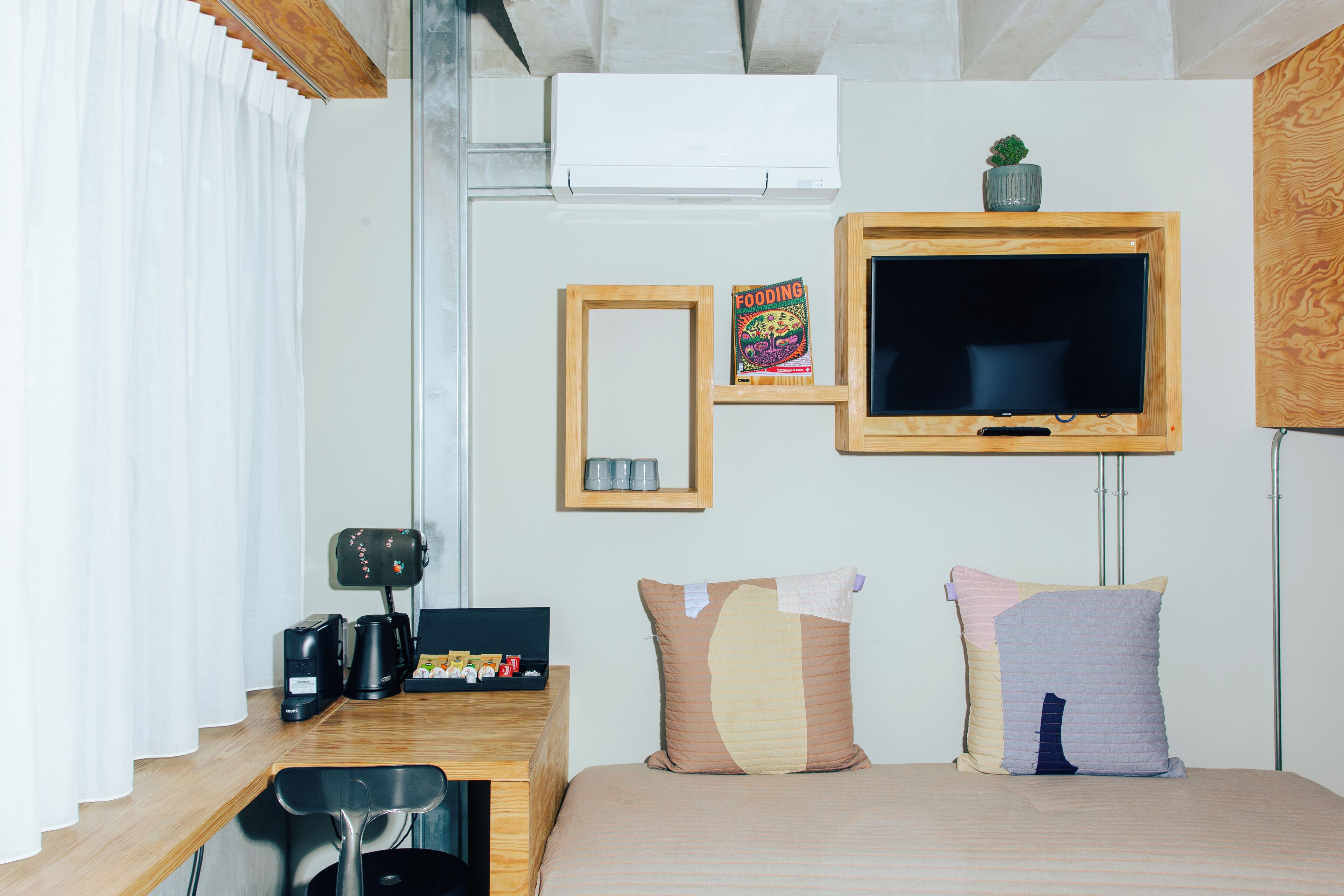 Habitación de hotel con cama, escritorio con cafetera, televisor y una pequeña planta en la pared.