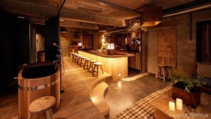 Un coin bar accueillant avec des tabourets en bois, un comptoir et un grand tonneau en bois.