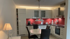 A modern kitchen with white cabinets, a dining table with chairs, a coffee maker, and a hanging light fixture.
