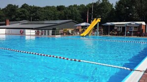 A swimming pool with lane dividers, a yellow slide, and a covered spectator area.
