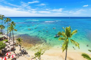 A beach with clear turquoise water, palm trees, and a few boats.