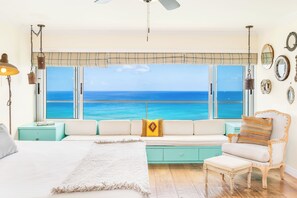A bedroom with a large window overlooking the ocean, a bed, a sofa, and a chair.