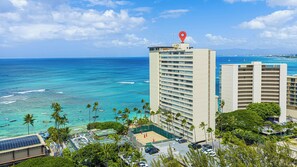 A high-rise hotel with a view of the ocean, a parking area, and palm trees.